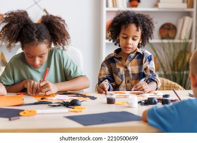 Happy Smiling Multinational Group Of Children  Making Halloween Home Decorations Together, Kids Painting Pumpkins And Making Paper Cuttings