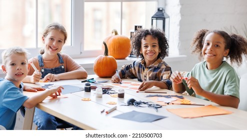 Happy Smiling Multinational Group Of Children  Making Halloween Home Decorations Together, Kids Painting Pumpkins And Making Paper Cuttings