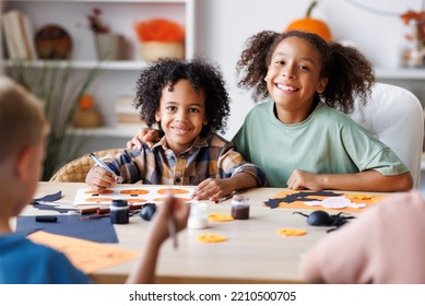 Happy Smiling Multinational Group Of Children  Making Halloween Home Decorations Together, Kids Painting Pumpkins And Making Paper Cuttings