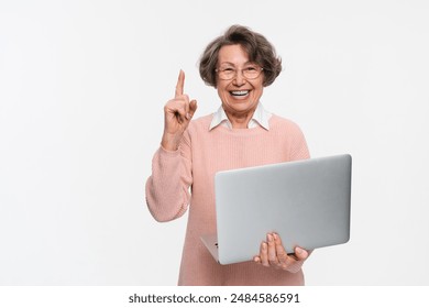 Happy smiling old senior mature woman grandmother in eyeglasses use holding netbook laptop indicate direct finger up empty space isolated on white color background. People and technology concept - Powered by Shutterstock