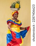 Happy smiling Palenquera fresh fruit street vendor dancing in the Old Town of Cartagena de Indias, Colombia. Cheerful Afro-Colombian woman in traditional clothing, Colombian culture and lifestyle.