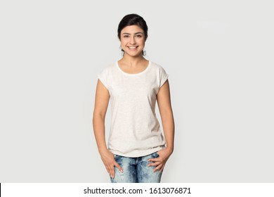 Happy Smiling Pleasant Indian Millennial Confident Woman Wearing White Mock Up T-shirt For Design Advertising With Copy Space For Promotional Text Looking At Camera Isolated On Grey Studio Background