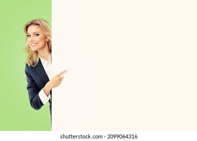Happy smiling pointing businesswoman grey suit standing behind blank banner or signboard billboard big bill board placard bigboard with copy space for text, isolated over light green color background.