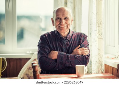 Happy smiling positive older man seated at table in kitchen room indoor. Grandpa inside of cottage home. - Powered by Shutterstock