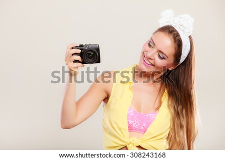 Happy smiling pretty pin up girl with hairband bow taking photo picture with camera. Attractive gorgeous young retro woman photographing.