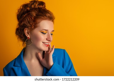 Happy Smiling Redhead Freckled Woman With Colorful Bold Eyes Makeup Posing On Orange Background. Copy, Empty Space For Text