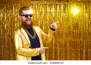 Happy smiling rich man in extravagant golden party jacket, gold chain and cool glasses with ginger beard and mustache pointing with finger to advertising copy space. Show, event, concert ad background - Powered by Shutterstock