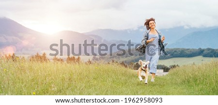 Happy smiling running beagle dog portrait with tongue out and owner female jogging by the mounting meadow grass path. Walking in nature with pets, happy healthy active people lifestyle concept image.