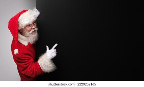 Happy smiling Santa Claus pointing with open hand palm at black banner with copy space for text - Powered by Shutterstock