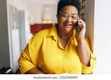 Happy smiling senior black plus size female in yellow shirt and glasses having nice conversation on phone with her best friend, smiling and laughing at jokes, sharing news and rumors - Powered by Shutterstock