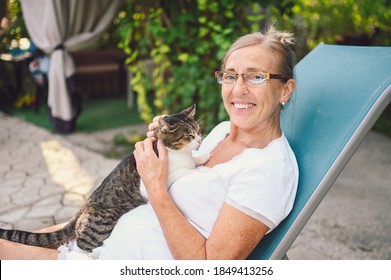 Happy smiling senior elderly woman in glasses relaxing in summer garden outdoors hugging domestic tabby cat. Retired old people and animals pets concept - Powered by Shutterstock