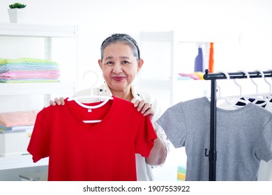 Happy Smiling Senior Elderly Woman Housewife Hanging Clothes Indoor To Dry, Older Asian Female Doing Laundry At Laundry Room, Dried Laundry, Grandma Doing Housework And Cleaning Clothes At House.