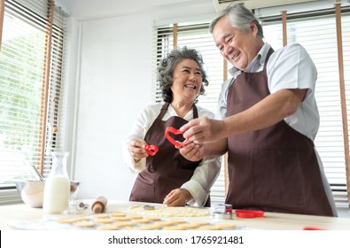 Happy Smiling Senior Lover man and woman baking in kitchen, Attractive Old couple enjoying holding red cookie cutter in heart shape while preparing and kneading dough at home together. Romance - Powered by Shutterstock