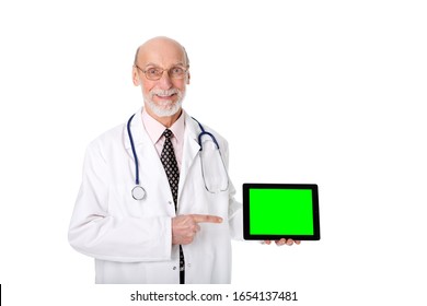 Happy, smiling senior man doctor aged 70-75 holding and pointing finger to tablet pc with green screen for copy-space ad text while looking at camera. Concept of medicine technology. Isolated on white - Powered by Shutterstock