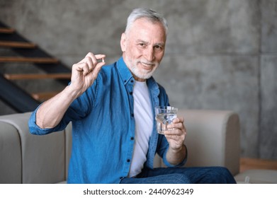 Happy smiling senior man taking supplements, daily vitamins for healthy lifestyle. Male holding tablet and glass with water. Intaking capsule with omega3, vitamin D - Powered by Shutterstock