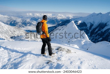 Happy smiling skier during active winter holidays. Man in winter clothing walking in snow and carrying ski on shoulder. Sporty man skiing with copy space of blue sky and snowy mountain.