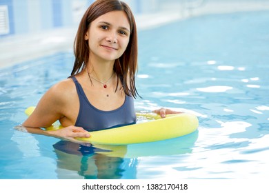 Happy Smiling Sportive Woman Doing Exercise In A Swimming Pool. Exercising In Swimming Pool With The Help Of A Aqua Tube. Young Healthy Female Doing Aerobics.