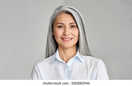 Happy Smiling Stylish Confident 50 Years Old Asian Female Professional Standing Looking At Camera At Gray Background. Portrait Of Sophisticated Grey Hair Woman Advertising Products And Services.