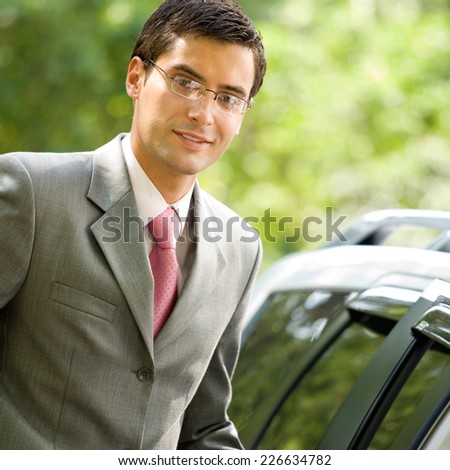 Happy smiling successful young businessman standing near new car, outdoor