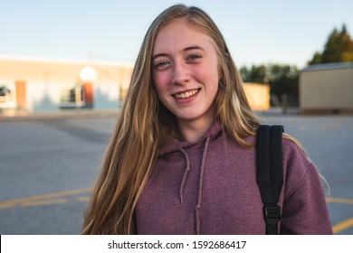 Happy smiling teen girl student standing outside of a school during sunset/golden hour while wearing a backpack. - Powered by Shutterstock