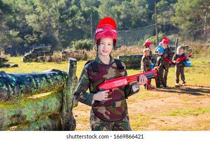 Happy  Smiling Teen Girl Wearing Uniform And Holding Gun Ready For Playing With Friends On Paintball Outdoor