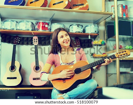 Happy smiling teenage girl posing with classical guitar in shop