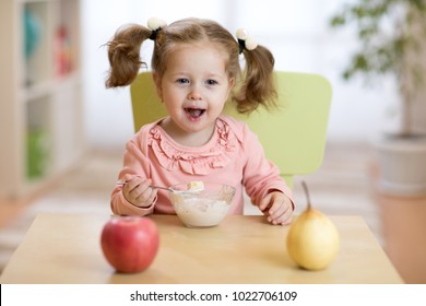 Happy Smiling Toddler Kid Eating Oatmeal With Fruits. The Concept Of Healthy Breakfast For Children.