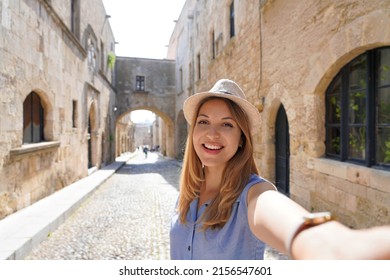 Happy Smiling Traveler Girl Taking Selfie In The Street Of The Knights Of Rhodes City, Greece. Young Female Traveler Visiting Southern Europe.