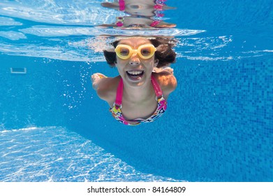 Happy Smiling Underwater Kid In Swimming Pool. Active Girl Swims And Having Fun. Child Sport On Summer Vacation