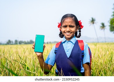 Happy smiling village girl kid showing green screen mobile phone while standing at paddy farmfield - concept of advertisement, app promotion and education