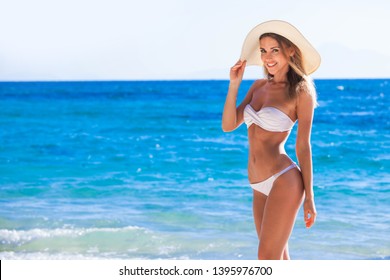 Happy lächelnde Frau in Bikini und Sonnenmütze am Strand