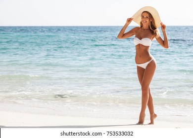 Happy smiling woman in bikini and sunhat on sea beach