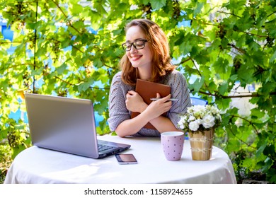 Happy smiling woman in black glasses digital nomad working on nature. Laptop, notebook, coffee and phone on the desk. Modern concept of online business, freelancing and remote work - Shutterstock ID 1158924655