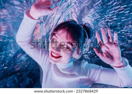 happy smiling woman with closed eyes and raised hands in white clothes and headphones dancing. Music lover. White dress code party, silent disco. Enjoy moment on shiny background. Selective focus