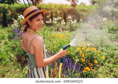 Happy smiling woman gardener in straw hat waters plants with hose pipe in summer garden. Taking care of flowers on farm - Powered by Shutterstock