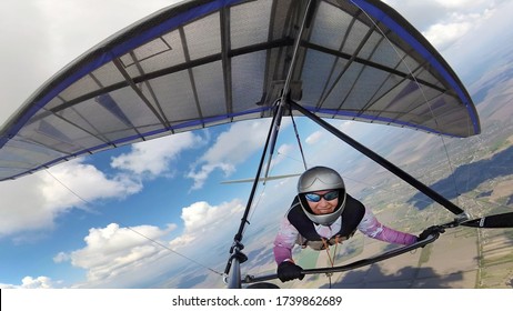 Happy smiling woman hang glider pilot high in the sky with cumulus clouds. Selfie by action camera