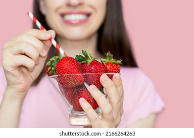 happy smiling woman holding glass bowl with fresh strawberries in hand and drinking straw in mouth.girl pretend to drink summer strawberry cocktail,juice,milkshake from fresh fruits.