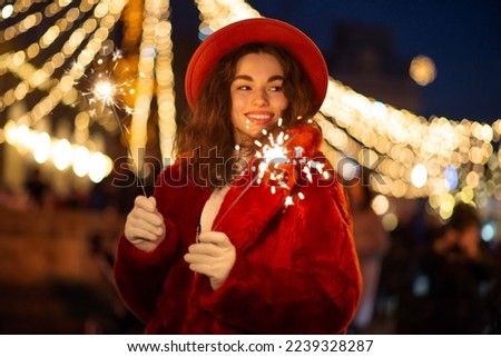 Happy smiling woman holding sparklers, posing at street festive Christmas fair in European city. Outdoor night portrait. Copy, empty space for text
