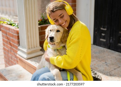 Happy Smiling Woman Listening To Music In Headphones In Yellow Sweater Walking At Her House With A Dog Golden Retriever Breed, Having Fun Together, Summer Style Casual Outfit