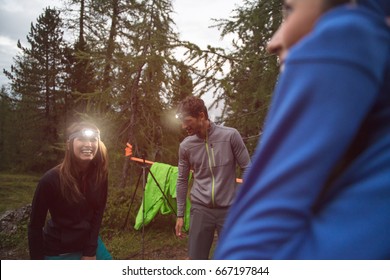 Happy Smiling Woman And Man With Headlamp Flashlight During Evening Near Camping. Group Of Friends People Summer Adventure Journey In Mountain Nature Outdoors. Travel Exploring Alps, Dolomites, Italy.