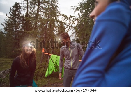 Happy smiling woman and man with headlamp flashlight during evening near camping. Group of friends people summer adventure journey in mountain nature outdoors. Travel exploring Alps, Dolomites, Italy.