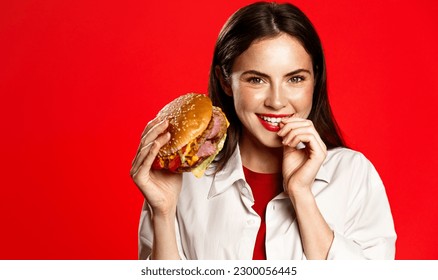 Happy smiling woman posing with cheeseburger, holding big tasty burger, enjoyment face, red background. - Powered by Shutterstock