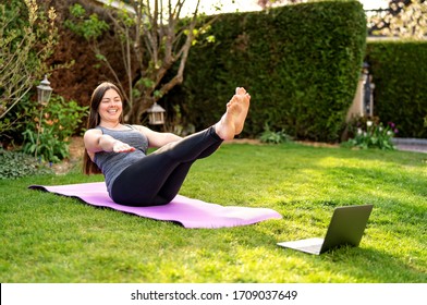 Happy smiling woman practicing pilates lesson online in garden outdoors during quarantine. Doing sport at home following guide or online tutorial or trainer instructions via skype