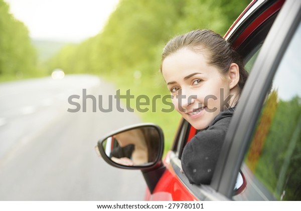Happy smiling woman in a red car. At sunset.\
Travel concept.