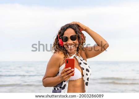 Happy smiling woman with red headphones and smartphone on beach landscape.Female using phone listening music on the seaside.