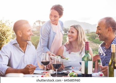 Happy smiling woman serving salad to friends and family outdoor in a sunset. Happy mature friends having dinner together. Senior men and middle aged women having fun while eating together at vineyard. - Powered by Shutterstock