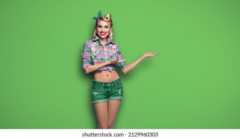 Happy Smiling Woman Showing. Excited Girl In Pin Up Style, Showing Advertising Something Or Copy Space For Ad Text. Blond Model - Retro Fashion And Vintage Hairdo Concept. Green Color Background