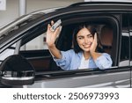 Happy smiling woman sitting in new car and holding keys in car dealership showroom