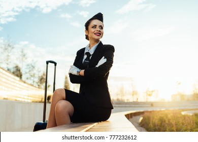 Happy Smiling Woman Stewardess In Uniform With Suitcase Waiting For Her Flight