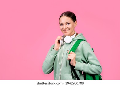 Happy Smiling Woman, Student Girl Goes To Study With A Backpack And With Headphones. Portrait On A Solid Monochrome Pink Background.